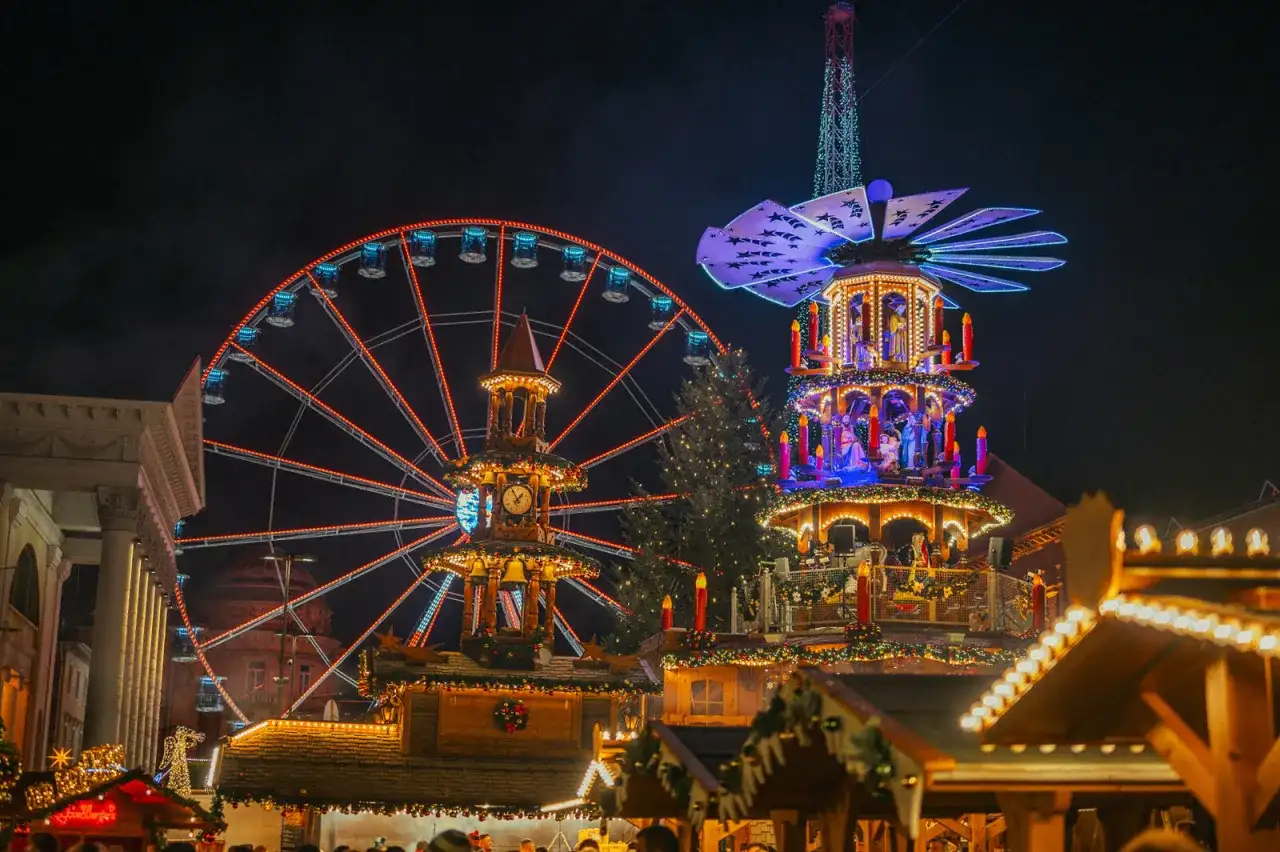 Ein beleuchtetes Riesenrad in Karlsruhe strahlt neben einer Weihnachts-Pyramide.