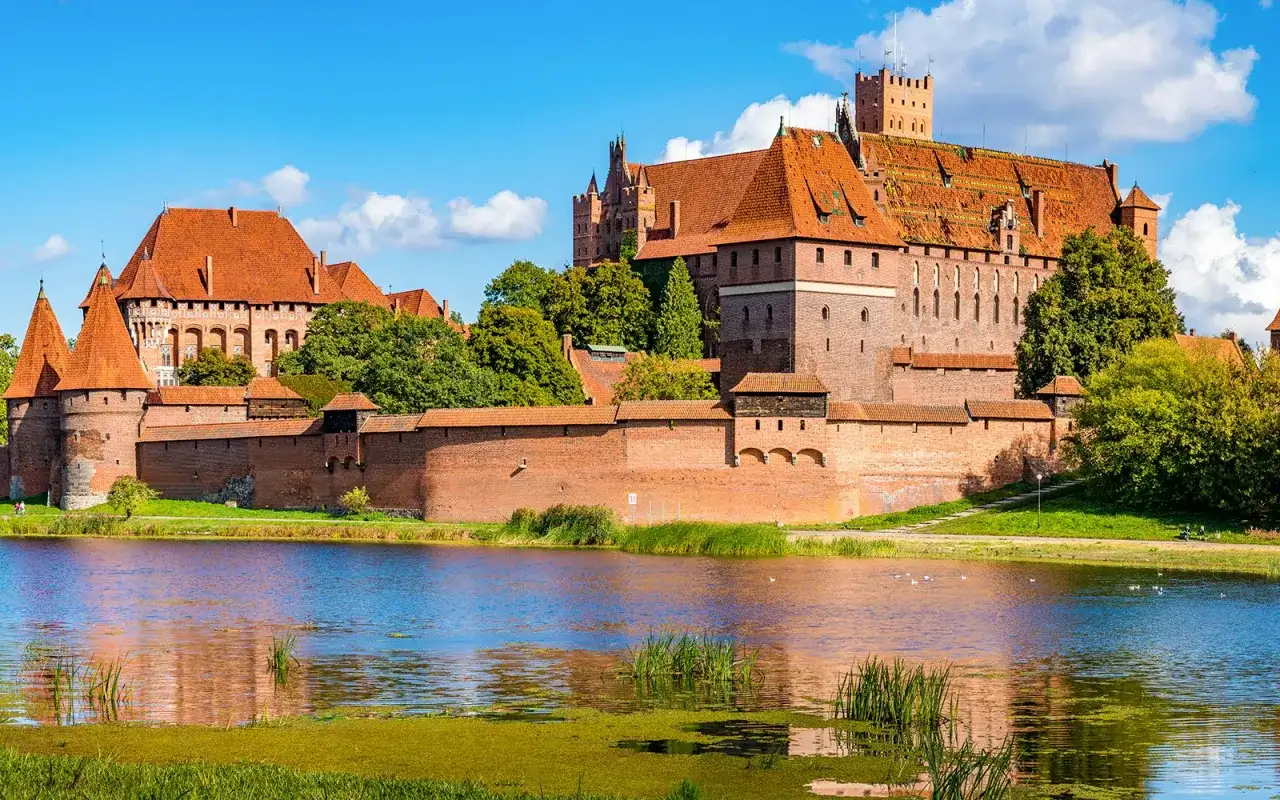 Die imposante Marienburg Burg, eine mittelalterliche Festung aus rotem Backstein, thront über einem ruhigen See.