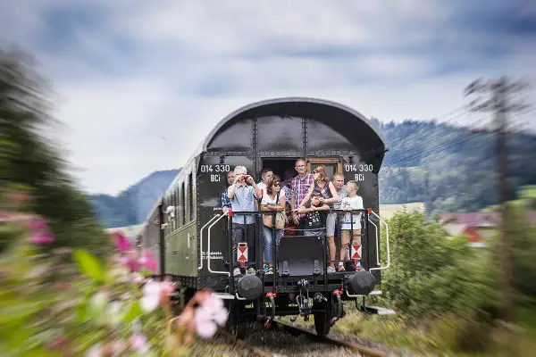 Familie genießt die Fahrt mit einem historischen Zug nach Polen. Blumen und grüne Hügel ziehen vorbei.