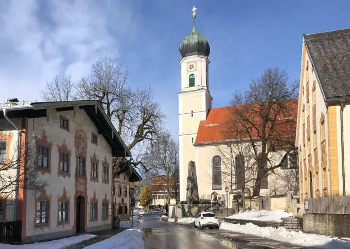 Winterliche Szene in Oberammergau mit der Pfarrkirche St. Peter und Paul. Die Fassadenmalerei der Häuser und die schneebedeckten Wege lassen die Vorfreude auf die passionsfestspiele oberammergau spüren.
